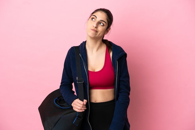 Foto jovem esportista caucasiana com bolsa esportiva isolada em um fundo rosa e olhando para cima