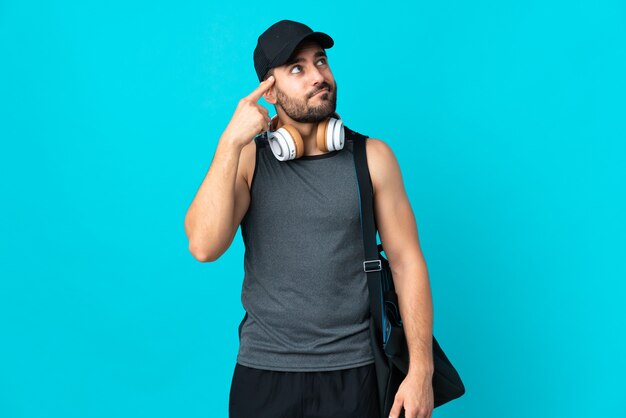 Jovem esportista com bolsa esporte isolada em azul fazendo o gesto de loucura colocando o dedo na cabeça