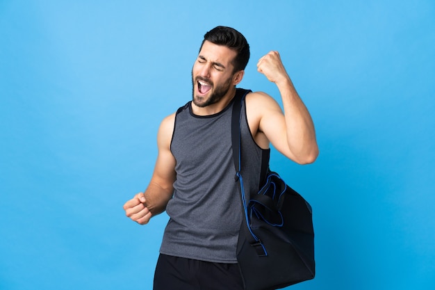 Jovem esportista com bolsa esportiva isolada em um fundo azul, comemorando uma vitória