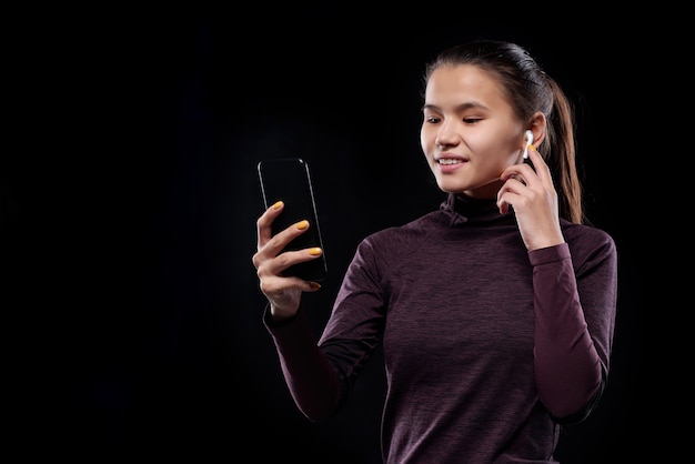 Jovem esportista com smartphone e fones de ouvido sem fio olhando para tela sensível ao toque