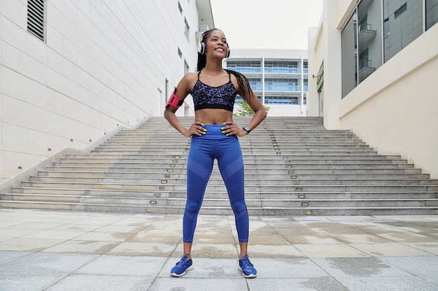 Jovem esportista em forma confiante em pé com as mãos na cintura e olhando para longe