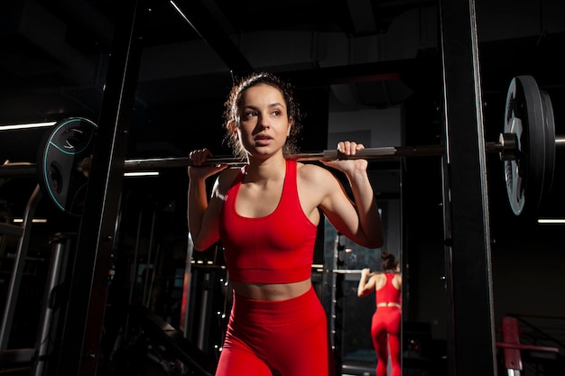 Jovem esportista em roupas esportivas vermelhas segura e levanta a barra nos trens de mulheres atléticas do ginásio