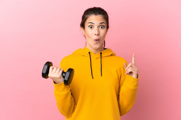 Jovem esportista fazendo levantamento de peso sobre um fundo rosa isolado com a intenção de perceber a solução enquanto levanta um dedo