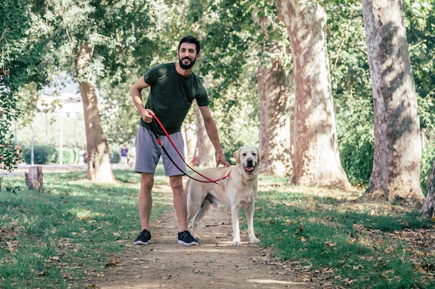 Jovem esportista passeando com seu cachorro labrador canadense por um parque urbano em um dia ensolarado