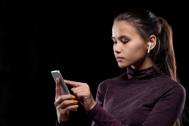 Jovem esportista séria com fones de ouvido sem fio apontando para a tela sensível ao toque do smartphone