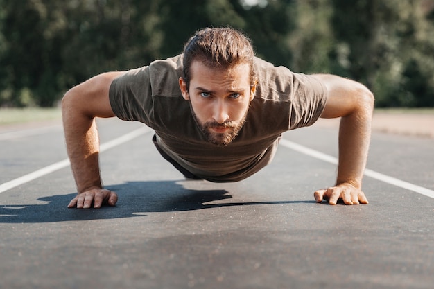 Jovem esportista sério fazendo flexões, praticando esportes ao ar livre, olhando para a câmera