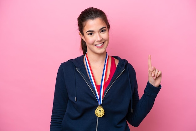 Jovem esportiva brasileira com medalhas isoladas em fundo rosa mostrando e levantando um dedo em sinal do melhor