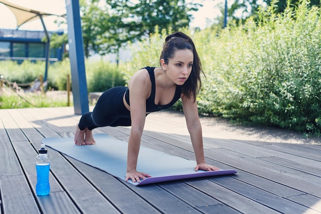 Jovem esportiva faz exercícios de ioga com tapete de ioga no conceito de estilo de vida ativo ao ar livre do parque