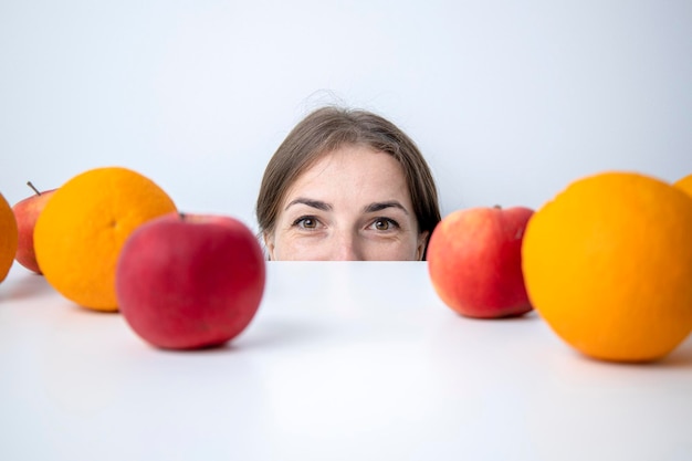 Jovem espreita debaixo de uma mesa na qual as frutas estão contra uma parede branca