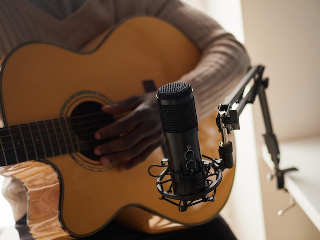 Jovem está cantando e tocando violão enquanto faz uma gravação de áudio em casa