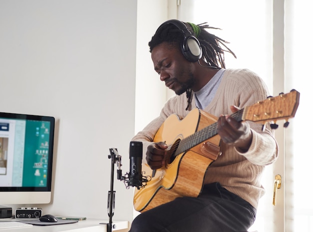 Jovem está cantando e tocando violão enquanto faz uma gravação de áudio em casa