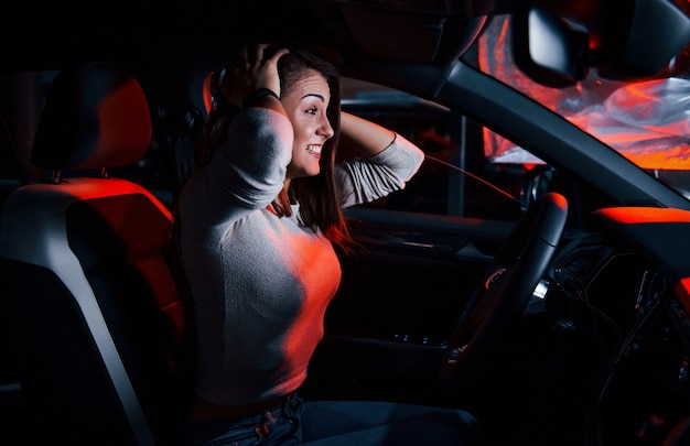 Jovem está dentro de um automóvel moderno novo com iluminação vermelha.