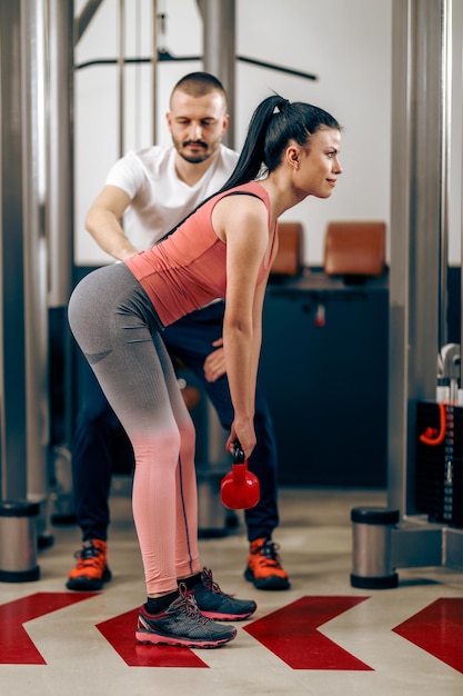 Jovem está fazendo exercícios com kettlebell durante o treino com personal trainer no ginásio.