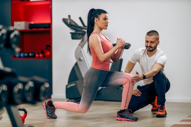 Jovem está fazendo treinamento para pernas com personal trainer no ginásio.