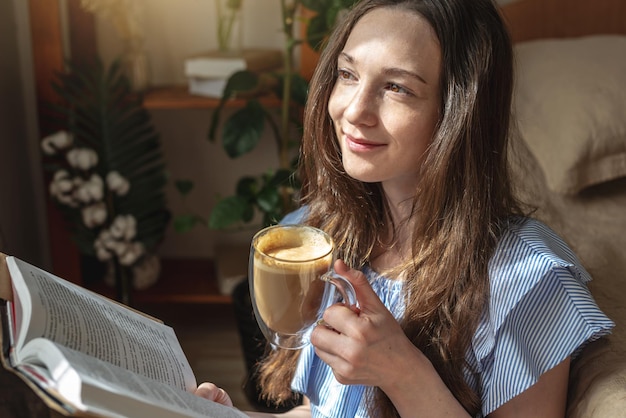 Jovem está lendo um livro e bebendo café sentado à janela Conceito de prazer matinal lazer passatempo agradável e relaxamento