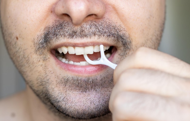 jovem está limpando os dentes com um fio dental de plástico palito fechar foto da boca