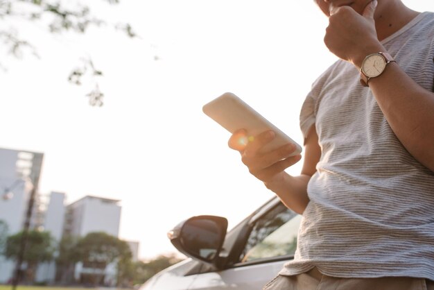 Foto jovem está perto do carro elétrico e olha para o telefone inteligente. o carro alugado está carregando na estação de carregamento para veículos elétricos. compartilhamento de carro.