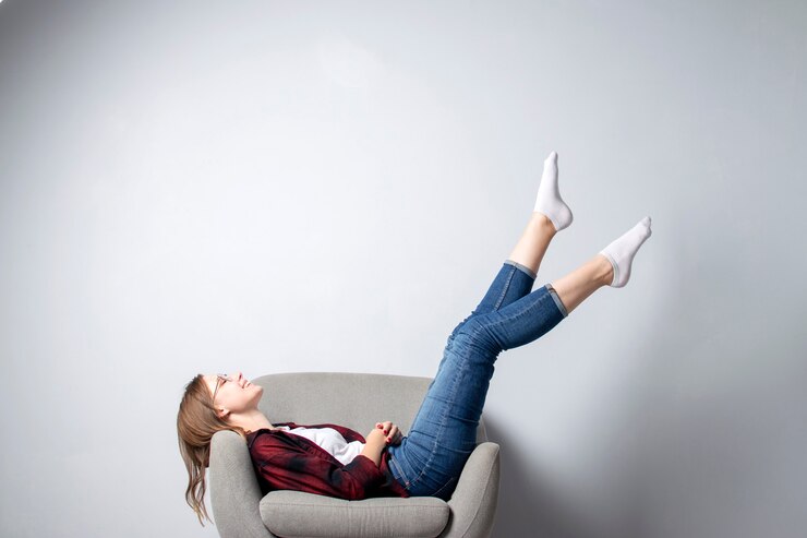 Foto jovem está sentado em uma cadeira macia e confortável contra uma parede branca com as pernas levantadas, um estudante de hipster está descansando e sonhando, copie o espaço