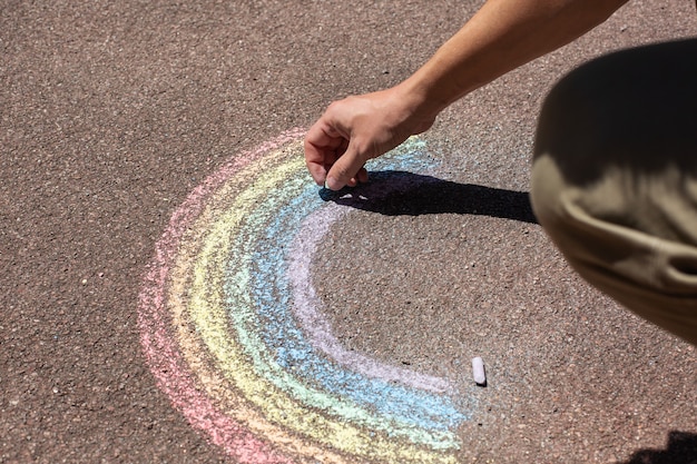 Jovem está sentado na calçada e desenhando o arco-íris durante o mês do orgulho. Liberdade, diversidade, aceitação, conceito LGBT