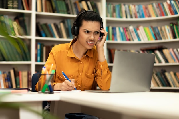 Jovem estudando online com laptop enquanto tem problemas auditivos em seus fones de ouvido sentados