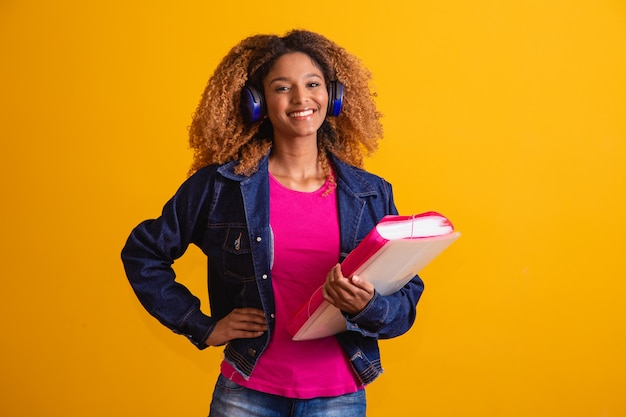 Jovem estudante afro com livros sobre fundo amarelo.