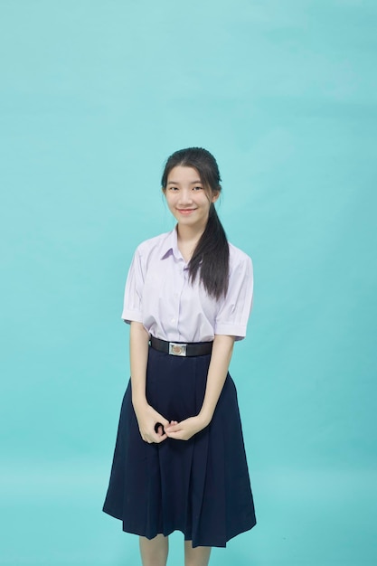 Jovem estudante asiática colegial com uniforme de estudante em fundo azul claro isolado.