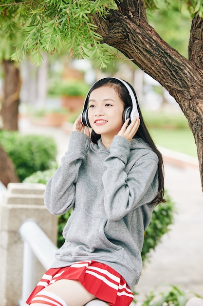 Jovem estudante asiática muito sorridente ouvindo música em fones de ouvido