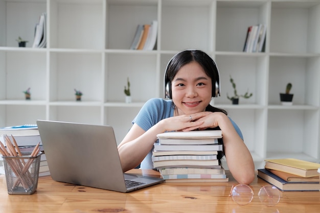 Jovem estudante asiática sorridente deitando a cabeça sobre a pilha de livros relaxando depois do estudo