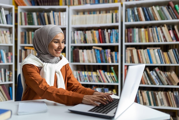 Jovem estudante bonita em hijab estudando online remotamente na biblioteca da universidade mulher digitando