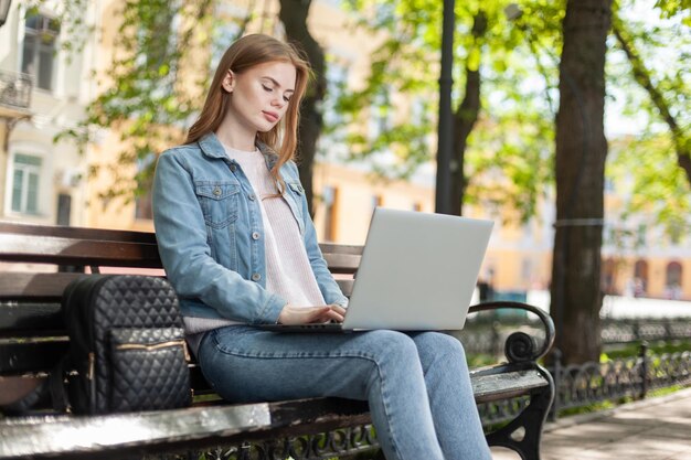 Jovem estudante bonita ou freelancer usando laptop enquanto está sentado em um banco na cidade