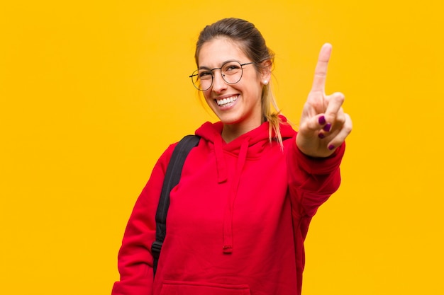 Jovem estudante bonita sorrindo e olhando amigável, mostrando o número onefirst com a mão para a frente, contando para baixo