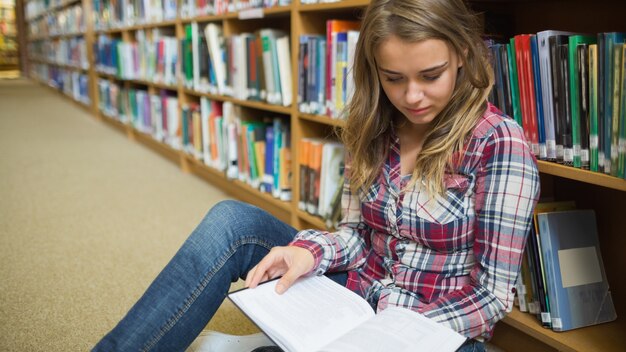 Jovem estudante bonito sentado no livro de leitura do chão da biblioteca