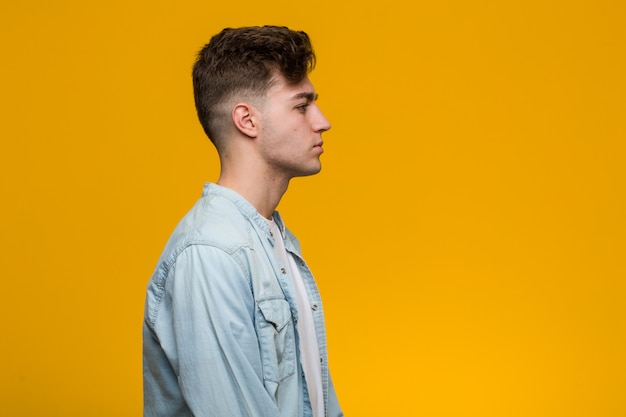 Jovem estudante bonito vestindo uma camisa jeans, olhando para a esquerda, posar de lado.