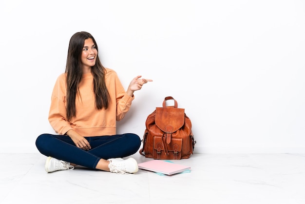 Jovem estudante brasileira sentada no chão apontando o dedo para o lado e apresentando um produto