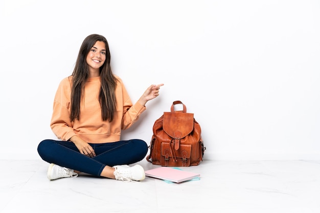 Jovem estudante brasileira sentada no chão apontando o dedo para o lado