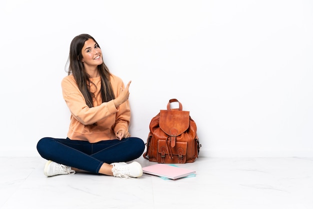 Foto jovem estudante brasileira sentada no chão apontando para trás