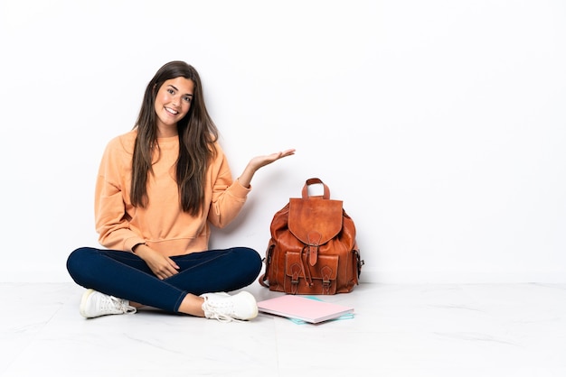 Jovem estudante brasileira sentada no chão apresentando uma ideia enquanto olha sorrindo para