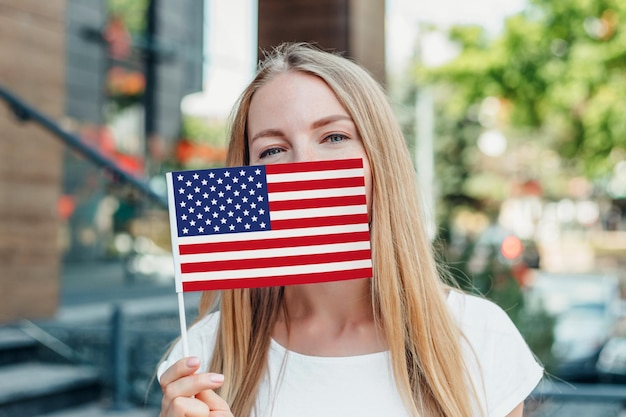 Jovem estudante cobre o rosto com uma pequena bandeira americana e se posiciona no contexto da universidade
