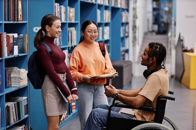 Jovem estudante com deficiência conversando com amigos no ambiente da biblioteca da faculdade