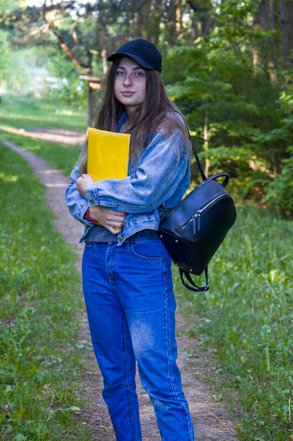Jovem estudante com pasta de olhos azuis e mochila no fundo da natureza