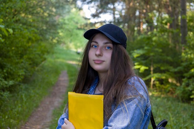 Jovem estudante com pasta de olhos azuis e mochila no fundo da natureza
