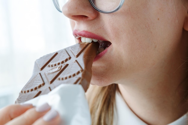 Foto jovem estudante comendo uma barra de chocolate de perto da boca comendo conceito de lanche não saudável