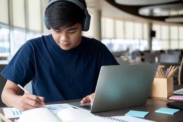 Jovem estudante de colagem usando computador e dispositivo móvel, estudando online.