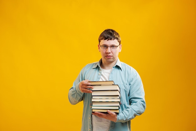 Jovem estudante de óculos segura pilha de livros universitários da biblioteca da faculdade em fundo amarelo Cara feliz sorri, ele está feliz em se formar no exterior conceito Espaço de cópia