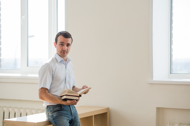 Jovem estudante do sexo masculino lendo livros na sala de aula ou sala de estar