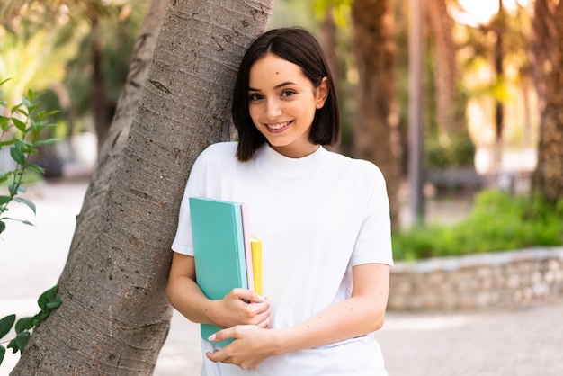 Jovem estudante feliz segurando cadernos ao ar livre