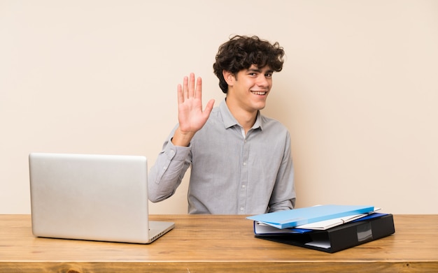 Jovem, estudante, homem, com, um, laptop, saudando, com, mão, com, feliz, expressão