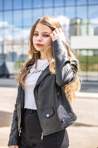 Jovem estudante loira de jaqueta de couro preta posando no estacionamento
