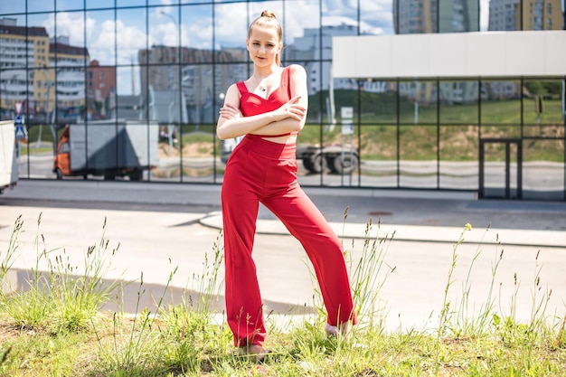 Jovem estudante loira de terno vermelho e jaqueta branca posando no estacionamento