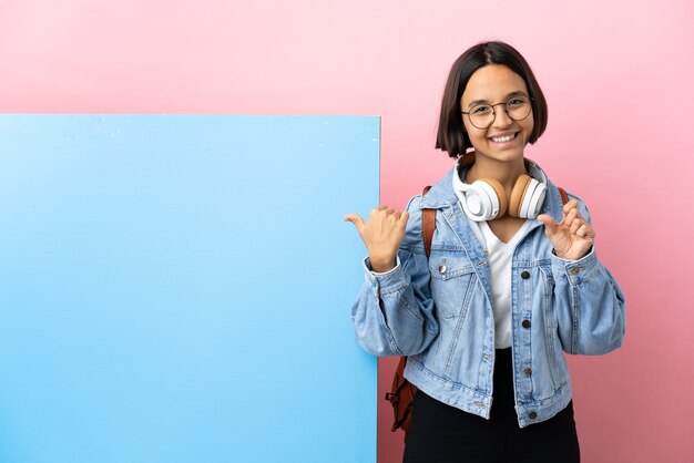 Jovem estudante mestiça com um grande banner isolado fundo apontando para o lado para apresentar um produto